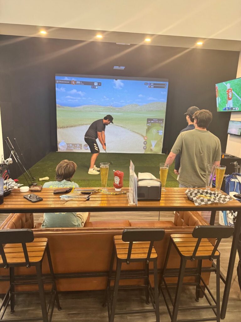 Golfer swinging in a golf simulator bay at Pin Point near North Myrtle Beach